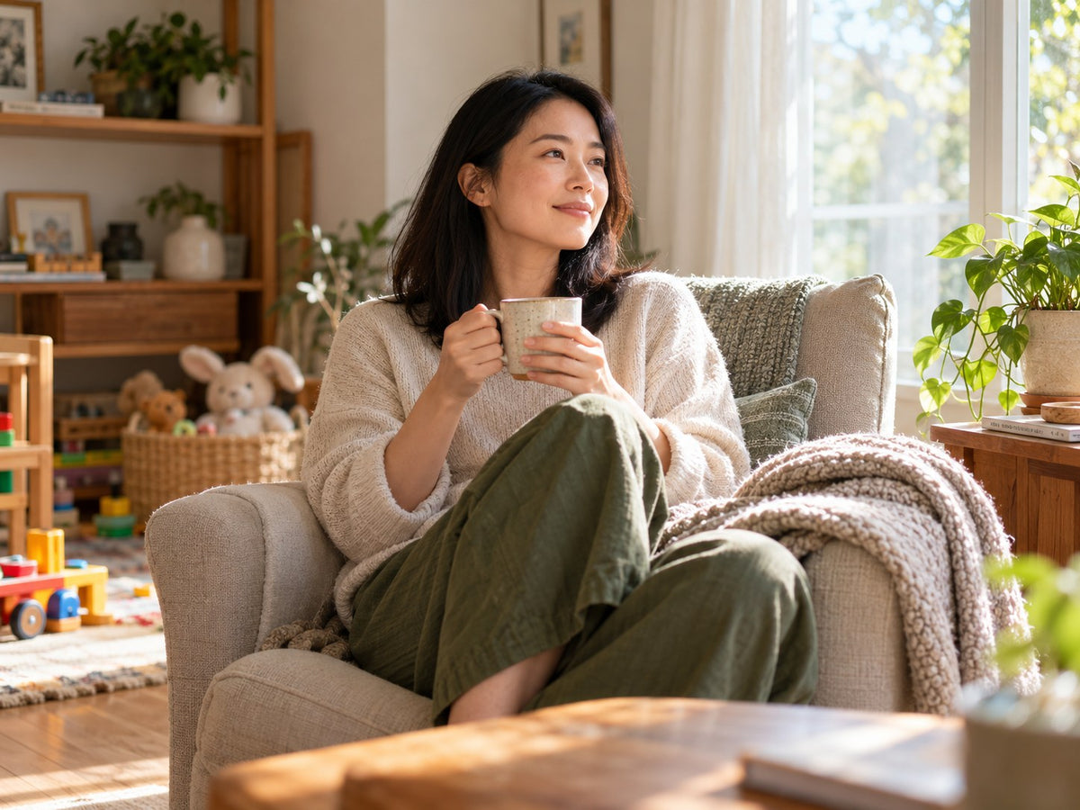 Mother taking a quiet midweek pause with a cup of tea beside a sunlit window.